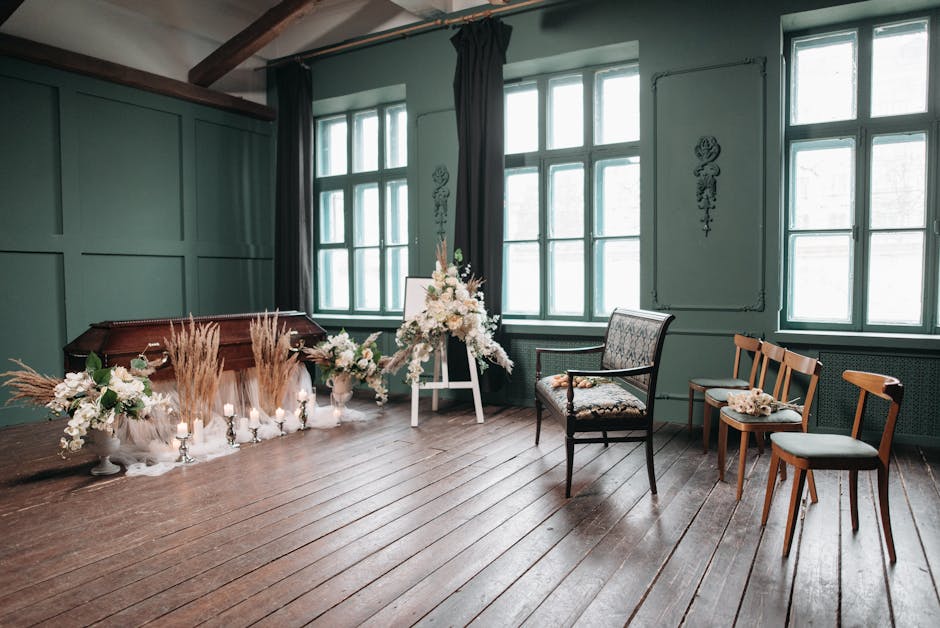 An interior setting with floral arrangements featuring white and cream-colored flowers, including roses and lilies, complemented by beige pampas grass and green foliage, arranged in white ceramic vase
