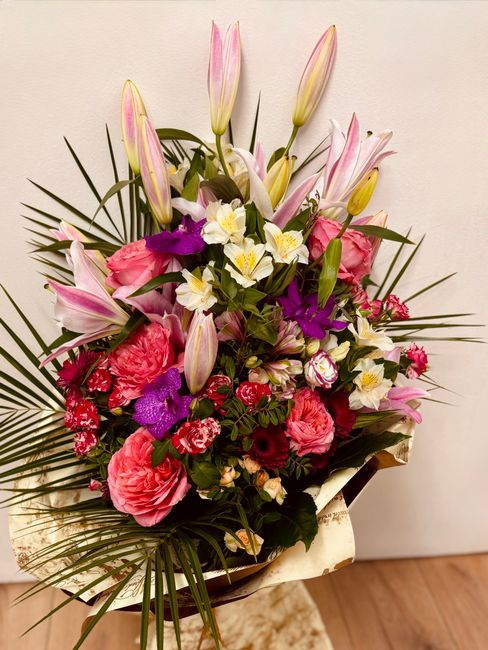 A vibrant floral bouquet arranged by flowersardleighgreen.co.uk, featuring a mix of fresh pink roses, white daffodils, purple orchids, and pink lilies with unopened buds, accented by lush green foliag